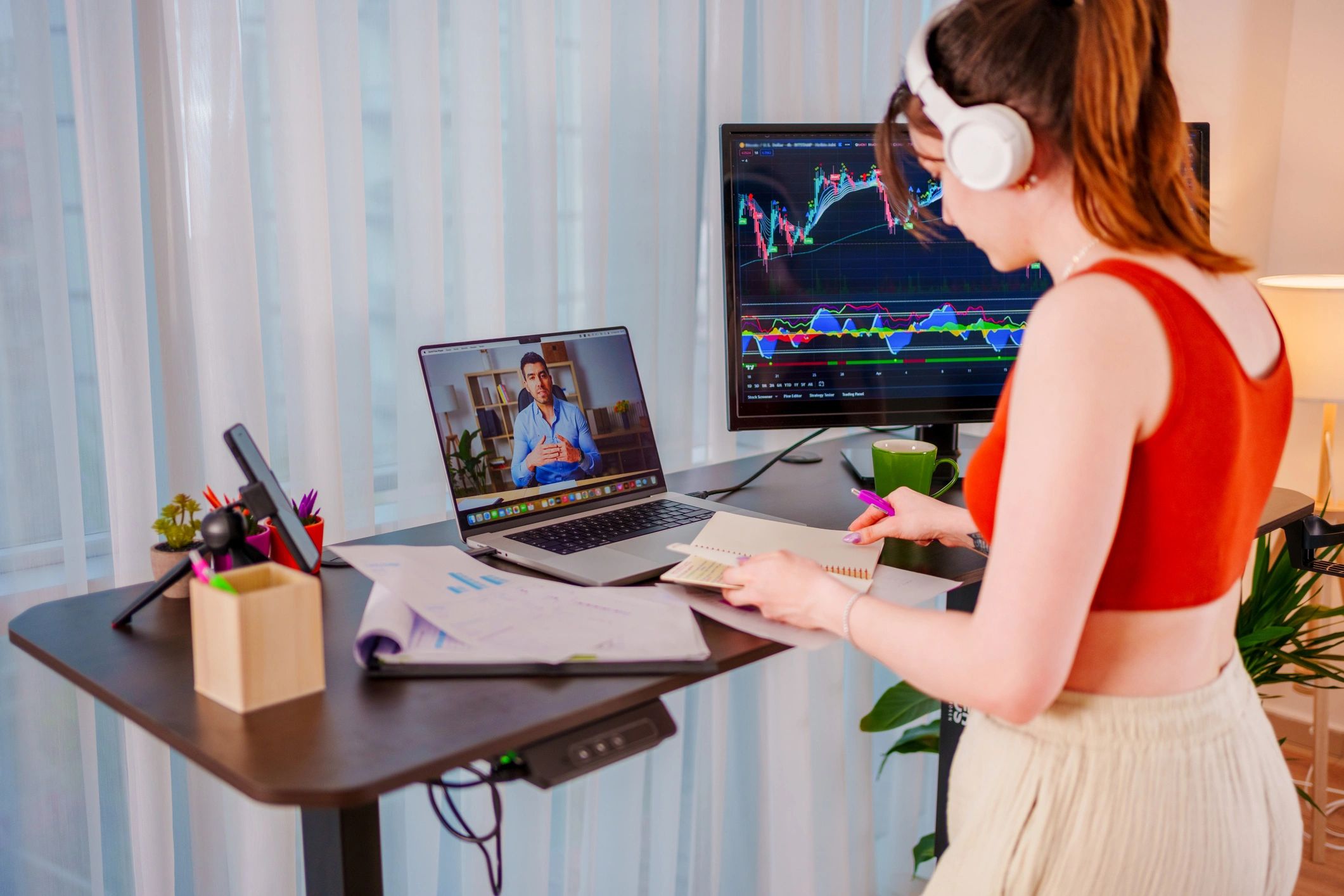 Young woman working from home at standing desk with online charts and virtual meeting